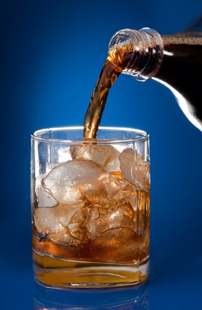 Filling glass with cola from a bottle on blue backgroundの写真素材