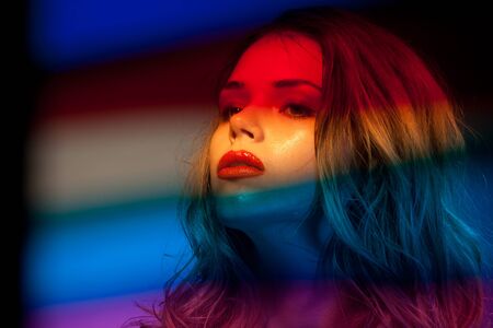 Beauty shoot of a beautiful female with blurry color filters on foreground with glossy skin and red lipsの写真素材