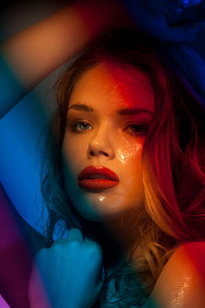 Beauty shoot of young woman expressing positivity and pleasure standing in shade of colorful lightの写真素材