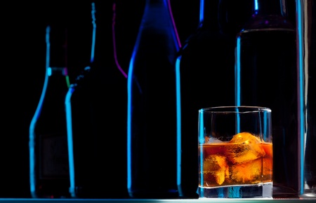 Row of bottles and shining alcohol drink in glass with iceの写真素材