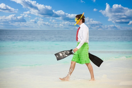 Businessman entering the ocean waters wearing snoring mask with flippers and wearing formal clothes with red tie entering water on the beachの写真素材