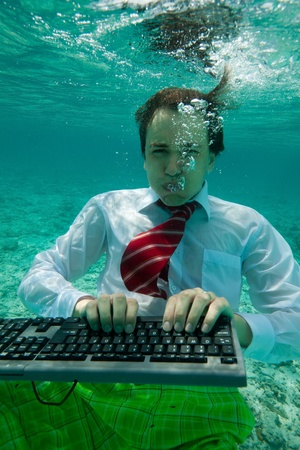 Young businessman with keyboard in formal clothes working underwaterの写真素材