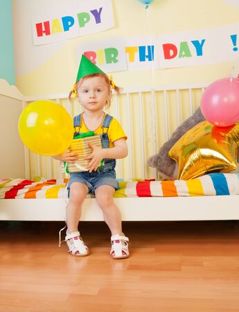 Little girl sit on the bed with birthday present and air balloonの写真素材