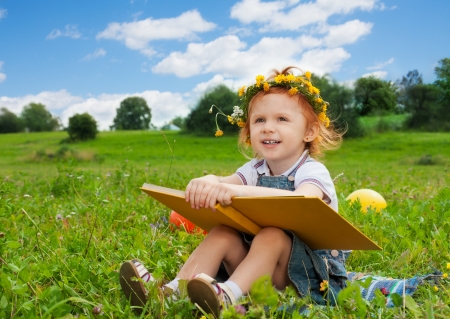 funny little girl reading book on the grassの写真素材