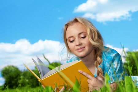 blonde girl laying on the green grass and readingの写真素材