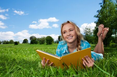 blonde girl laying on the green lawn and reading and dreamingの写真素材