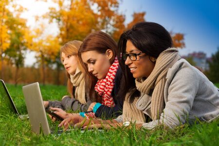 three students browsing in autumn parkの写真素材