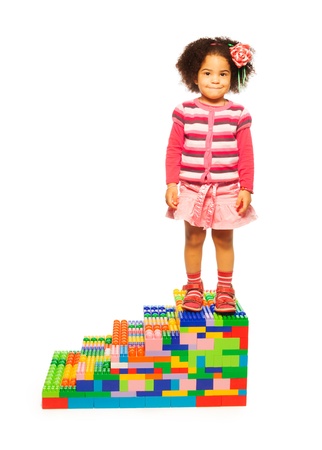 Dark girl standing on toy stairs made of plastic blocksの写真素材