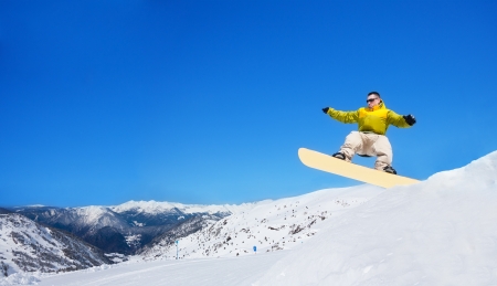 Cute handsome snowboarder man jumping from trampoline on snowboard in ski park in mountain resortの写真素材