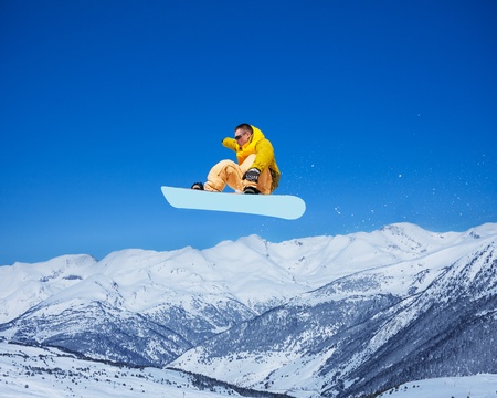 Cool handsome snowboarder man holding snowboard in the air jumping with mountains on backgroundの写真素材