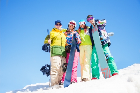 Four happy friends hug and hold snowboards standing in snow in winterの写真素材