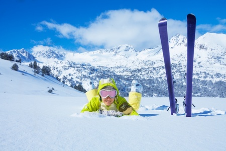 Young happy woman laying in snow with her ski standing by with mountain on backgroundの写真素材