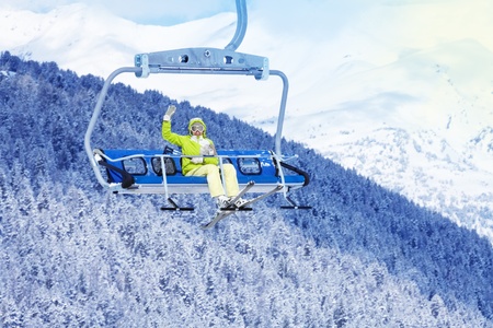 Happy skier young woman sit on the ski lift and waiving handの写真素材
