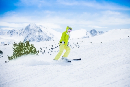 Yong happy woman ski downhill with snow powder flying from her, with mountain peaks on the backgroundの写真素材