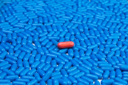 One red drug pill laying on many blue tablets