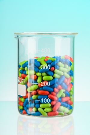 Laboratory glass container with green blue and red tablets and pills on blueの写真素材
