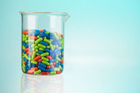 Laboratory glass container with green blue and red tablets and pills on blue and copyspaceの写真素材