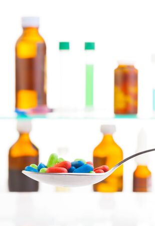 Spoon full of pile of color drugs and cold mixture with different drugs in jars, bottle and test tubes standing on shelf with medicineの写真素材