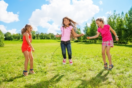 Three girls jumping over the rope in the park, having fun in active games outsideの写真素材