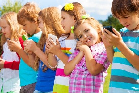 Beautiful group of many kids standing with cell phones talking texting and playing, all outsideの写真素材