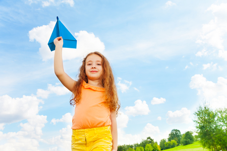 Cute happy 6 years old Caucasian girl with blue paper airplane on bright sunny dayの写真素材