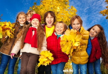Group of seven kids around 10 years old , boys and girls, standing together in the park with autumn yellow maple tree on backgroundの写真素材