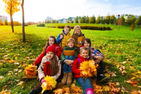 Group of happy kids sit in the park on the grass holding bouquets of autumn maple leaves and smilingの写真素材