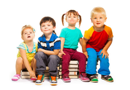 Four little kids sitting on the the stack of books isolated on whiteの写真素材