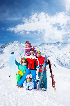 Group of happy excited smiling 2 men and 3 women with snowboards and skis wearing goggles standing and posing on the mountains backgroundの写真素材