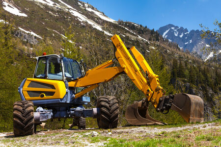Yellow excavator working near mountains in summerの写真素材