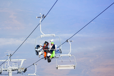 Three snowboarders sitting on ropeway and lifting highの写真素材