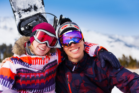 Hugging couple in ski masks together on the snow with snowboard behindの写真素材