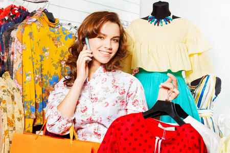 Smiling  girl talking on mobile and shopping in the mall while carrying bags and clothes