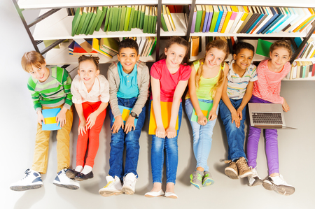 Portrait from above of seven smiling children sitting together on floor and looking up with heads upの写真素材