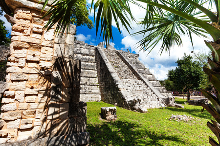 View of stoned wall and Chichen Itza monument, Mexico and palms around in summer