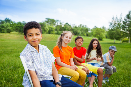 Five happy friends sit on chairs in row outdoorsの写真素材