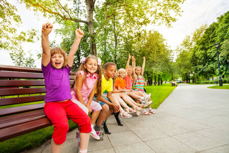 Kids in row on bench with some mates excitedの写真素材
