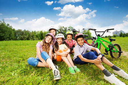Happy kids in helmets sit on grass and smileの写真素材