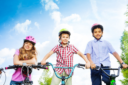 Three kids in helmets hold bike handle-barsの写真素材