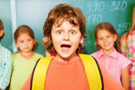 Portrait of excited boy with bag near chalkboard