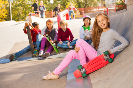 Girl with skateboard and friends sitting behindの写真素材