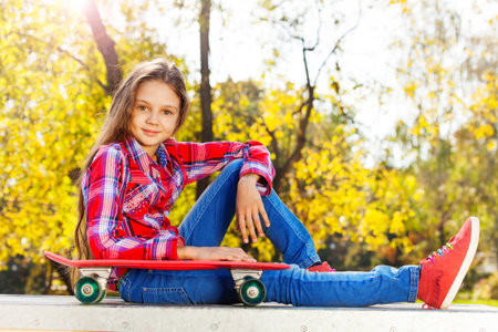 Smiling girl sitting with her arm on skateboardの写真素材