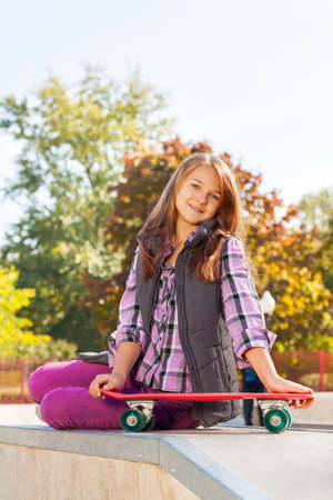 Positive girl holds skateboard sits on groundの写真素材