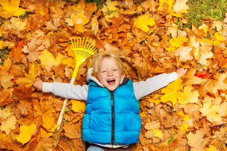 Laughing boy laying on the autumn leaves with rake Laughing boy laying on the autumn leaves with rake