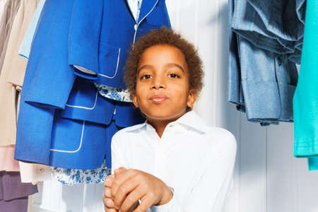 Cute African boy in white shirt sits under hangersの写真素材