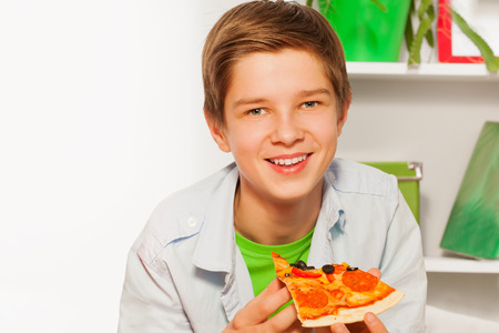 Happy boy holding pizza piece and eating at homeの写真素材