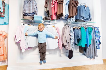 Cute boy stands among clothes on hangers and shelfの写真素材