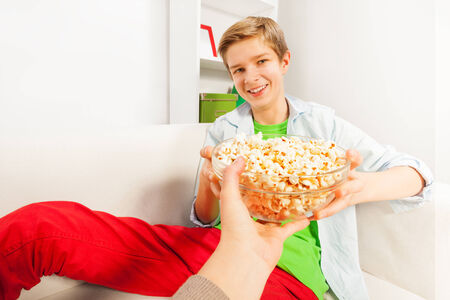 Smiling boy holds popcorn bowl from someones handの写真素材