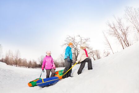Children walking up the snowy hill and carry tubes