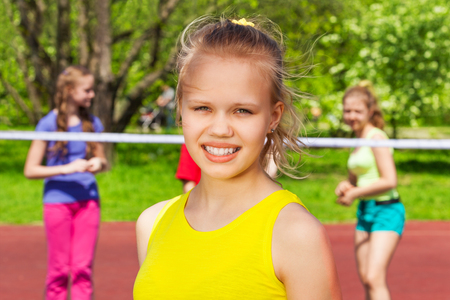 Portrait of blond teen girl with friends playing behind in volleyball on the playground during sunny summer dayの写真素材